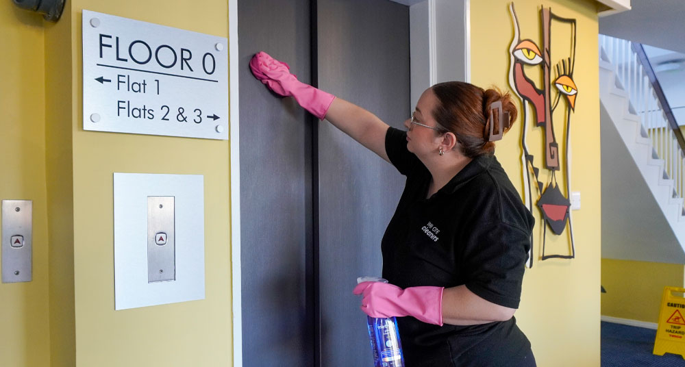 woman cleaning lift doors in an apartment block